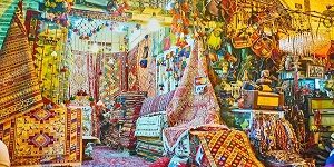 SHIRAZ, IRAN - OCTOBER 12, 2017: Scenic carpet stall with colored kilims and rugs, covered with patterns, neighbors with antique stall with different souvenirs and jewelries, Vakil Bazaar, on October 12 in Shiraz.